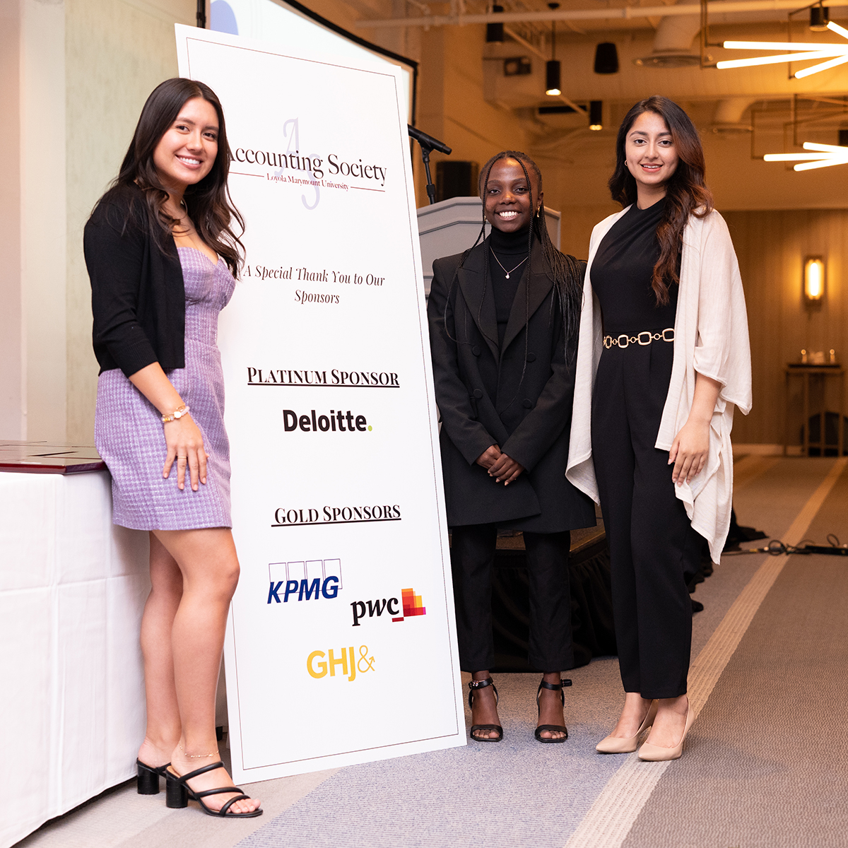 Three students in professional dress in front of a banner with the LMU Accounting Society, Deloitte, KPMG and PwC logos.